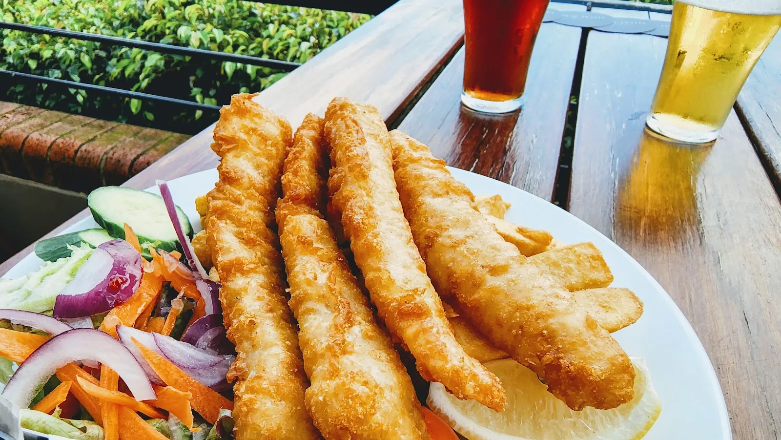 Battered fish fillets with salad, beside two beers on an outdoor table