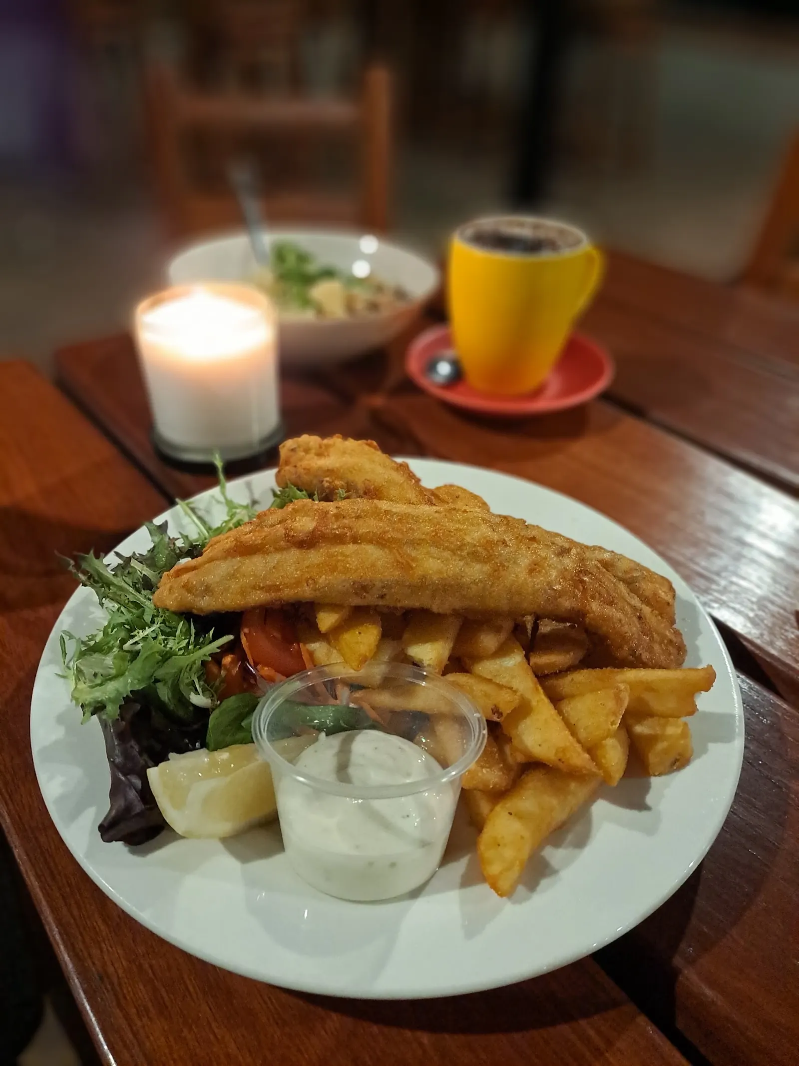 Battered fish with chips, salad and tartare sauce, a candle on the table behind